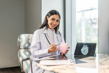 Portrait of a smiling female doctor cardiologist showing model of the heart and looking at the camera in a hospital office or clinical examination room, Healthcare and medical service