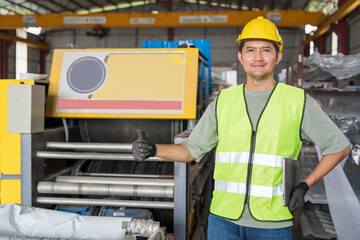 Happy Asian engineer in high-vis vest and hard hat giving a positive thumbs-up in front of a heavy industrial roll forming machine.