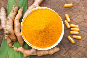 Turmeric Powder in a Bowl with Fresh Rhizomes and Capsules on Wood Background