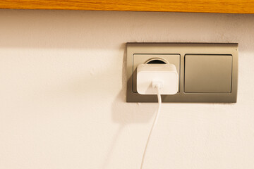 Grey plug used with a charger on the white wall.