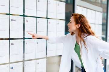 Woman pointing at listings on a display board outside a real estate office in a city during the day