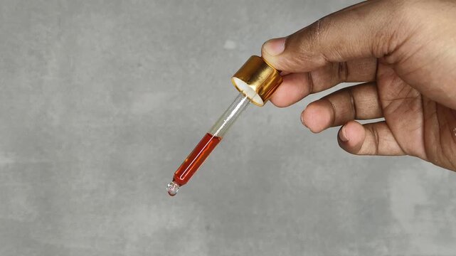 Closeup of hand with transparent medicine millilter dropper or medical filler and red color liquid dripping isolated on white background with copyspace. Serum or essential oil treatment concept.