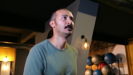 Man with mustache running on a treadmill in the gym. Diagonal front view of an athlete in his 30s doing a cardio workout, wearing a t-shirt. 4K.