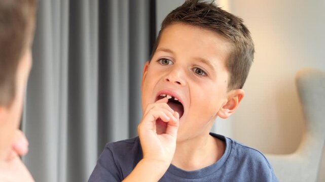 Little boy trying to pull out central incisor tooth that is about to fall out. Close up
