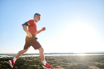 Senior man running on the beach wearing sport clothes and earphones