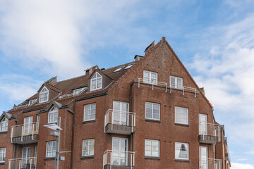 Red brick apartment building with balconies and dormer windows under blue sky. Classic northern German urban housing design.