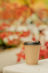 Paper coffee cup on a concrete table surrounded by colorful autumn leaves, cozy fall atmosphere.