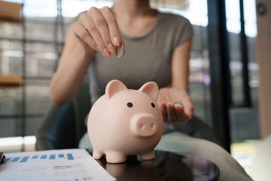 Woman writing financial plans in a notebook beside a piggy bank and coins on a table, symbolizing budgeting and savings management.