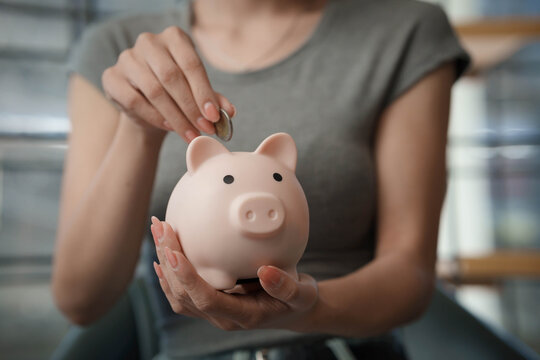 Woman writing financial plans in a notebook beside a piggy bank and coins on a table, symbolizing budgeting and savings management. - Powered by Adobe