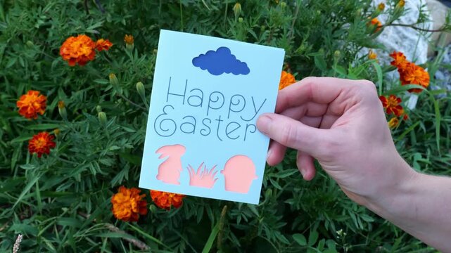 Woman Holds Up Handmade Happy Easter Card with Bunny Rabbit and Egg Basket in front of Orange Marigold Flowers 4K Video Stock Footage
