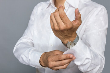 A close-up of a man's hands, buttoning buttons, cufflinks on a snow-white shirt, and an elegant watch on his wrist.