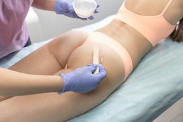 Girl in a beauty salon. Preparing for the procedure. Beautician applies the gel to girl bottom. Concept of body care, hygiene, skin, hardware cosmetology.