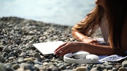Beach Girl Reading Book: Woman reads a book, relaxes on pebble beach during sunny summer day.