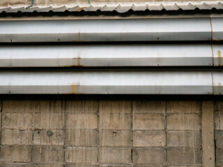 Old weathered concrete block wall with rusty corrugated metal siding and zinc roof showing deterioration and water stains