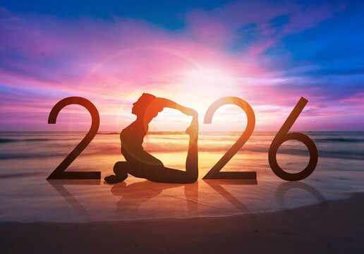 Happy new year card 2026. Silhouette of healthy girl doing Yoga One Legged Pigeon pose on tropical beach with sunset sky background, woman practicing yoga as a part of the Number 2026 sign.