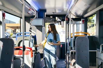 Young woman taps a contactless card to pay bus fare while commuting through a sunlit city bus...