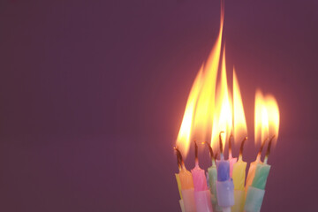 Several different birthday cake candles burning on purple background. Copy space for text.