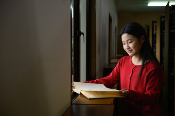 Naklejka premium An Asian girl is reading a book in a library