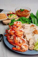 Shrimp and pork belly served with fresh vegetables and delicious dipping sauce, served as a set on a white table.