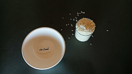 Conceptual image showing an empty bowl with a note “No Food” beside a glass filled with rice,...