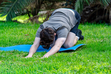 Man stretching body in child's pose on green grass