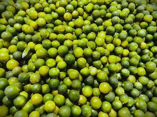 Overhead macro close-up of a massive, dense pile of small, vibrant green calamansi limes or key...