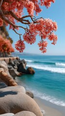 Macro Shot Of Tropical Buds In Bloom With Vibrant Petals Hanging From A Branch Overlooking A Blue Ocean And Rocky Shoreline Under A Clear Sky