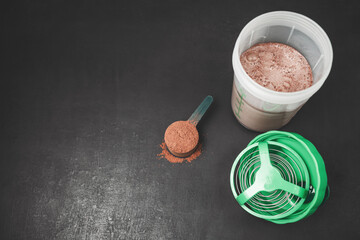 Chocolate whey protein powder scoop and protein shake in shaker bottle on dark background with copy space, sport nutrition concept