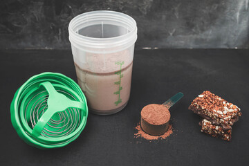 Chocolate whey protein powder scoop, protein shake in shaker bottle and protein bar on dark background, sport nutrition concept