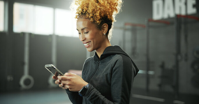 Woman, gym and smile with phone for social media, message or online post and break. Happy african person, sports center and fitness with laugh on internet for funny video, meme or notification - Powered by Adobe