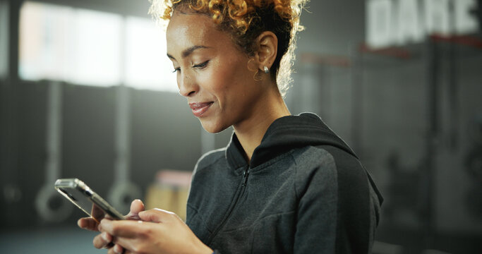 Woman, gym and reading with phone for social media, message or online post and break. Happy african person, sports center and fitness with smile on internet for tutorial, chatting or notification