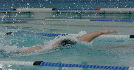 Swimming athlete performing front crawl stroke in pool lane, with cap, goggles and lane dividers