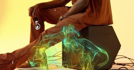 Sitting sideways man wearing rust outfit on black box in studio, with glowing wireframe projection