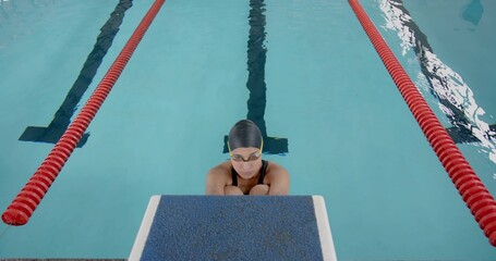Swimmer wearing black swimsuit, cap and goggles gripping block at pool with red lane dividers