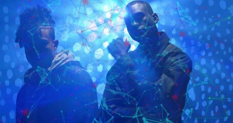 Posing two men wearing hoodie and zip-up jacket in blue studio, with glowing network bokeh overlay