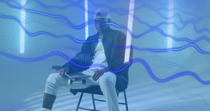 Holding skateboard skateboarder sitting on stool in studio, with neon tubes and blue wave trails - Powered by Adobe