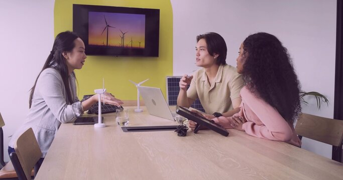 Collaborating team in boardroom wearing formal wear discussing renewable energy with scale models
