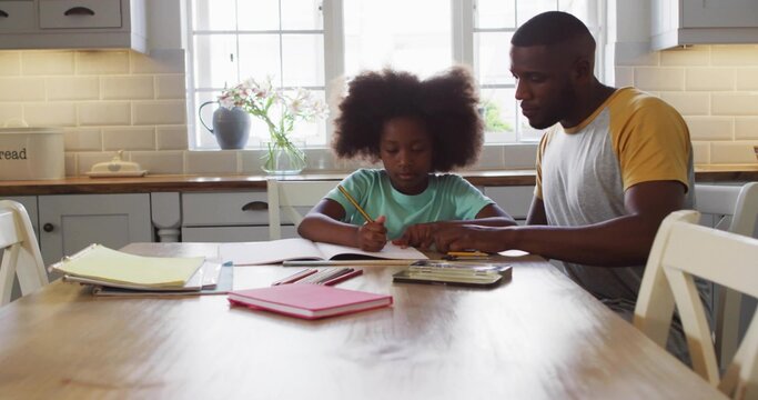 Teaching father and daughter doing homework at kitchen table, with notebooks and colored pencils - Powered by Adobe