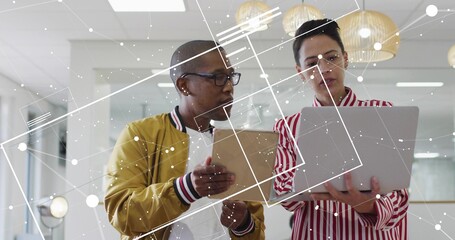 Comparing tablet-holding coworker and laptop-holding peer analyzing data in office, network overlay