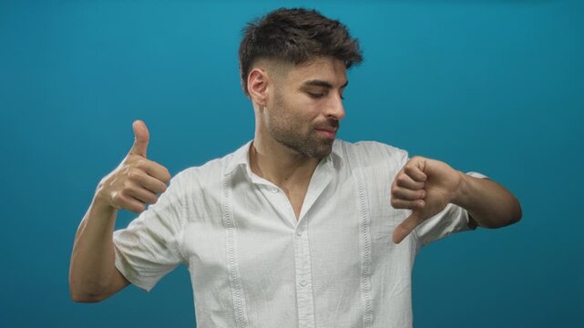 Man hand showing thumbs up and thumbs down in blue studio; indecision.
