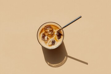 Glass of iced coffee with stainless steel straw casting long shadow on warm beige background under natural afternoon light.