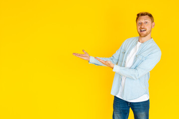 Studio portrait of a cheerful man smiling and presenting an inviting gesture against a bright yellow background, exuding confidence and warmth