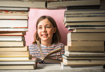 Child girl reads a book with a pile of books beside her.