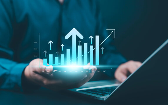 Businessman using laptop and smartphone with digital bar chart and upward arrows, representing business growth, success, financial performance, investment, analytics, and technology-driven progress