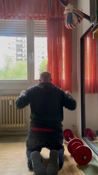 hombre deportista de rodillas con pesa y mancuerna celebrando y suspirando en gym de casa