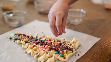 Close-up of a child’s hand decorating cookies with colorful sprinkles. Fun and creative baking activity for kids at home, representing family bonding and creativity.
