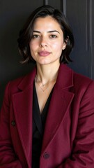 Fototapeta premium a brunette woman with short hair wearing a dark red bordeaux coat on a black wall background, fashion photography, fall winter collection