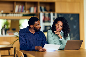 African-American Man and African-American Woman Collaborate Over Documents and Laptop in Library Setting