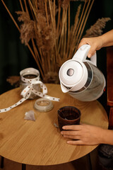 Making tea at home: a woman takes tea bags out of a jar next to an electric kettle