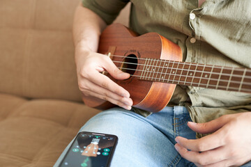 man playing ukulele with smart phone on sofa at home